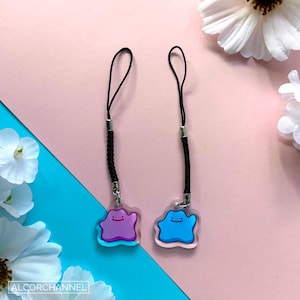 May include: Two clear plastic charms with black string phone straps. The charms are shaped like the Pokemon character,  Jigglypuff. One charm is purple and the other is blue.