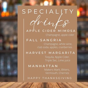May include: A tan sign with the words "SPECIALITY drinks" in white. The sign lists drink recipes: Apple Cider Mimosa, Fall Sangria, Harvest Margarita, and Manhattan. The words "Happy Thanksgiving" are at the bottom.