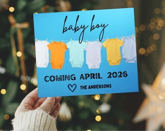 May include: A blue card with the words "baby boy" in cursive script. Below, it reads "COMING APRIL 2026" and "THE ANDERSONS" with a heart symbol. The card features baby onesies in various colors.