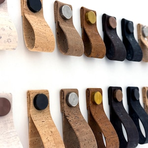 Puede incluir: Una colección de 18 tiradores de armario diferentes en varios colores y materiales. Los tiradores están hechos de corcho, cuero y metal. Algunos de los tiradores tienen un diseño simple, mientras que otros tienen un diseño más intrincado.