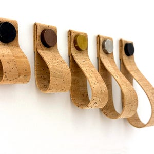 Peut inclure: Cinq poignées de tiroir en cuir de liège avec des accents métalliques de différentes couleurs. Les poignées sont alignées, l'accent noir à gauche et l'accent argent à droite.