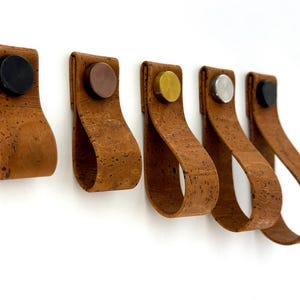 Può includere: Cinque tiretti per cassetti in sughero con accenti metallici di diversi colori. I tiretti sono marroni e hanno una superficie testurizzata.