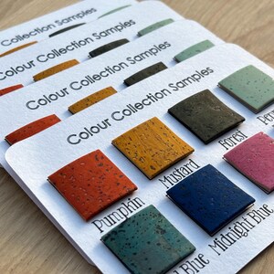 May include: Close-up of several white cards labeled "Colour Collection Samples" with various colored cork samples. Colors include pumpkin, mustard, forest, midnight blue, and fuchsia. The cards are arranged on a light wood surface.