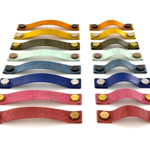 Peut inclure: Un ensemble de 10 poignées de tiroir en liège de différentes couleurs, dont le jaune, le vert, le bleu et le rouge. Chaque poignée a une forme incurvée et deux boutons métalliques à chaque extrémité.