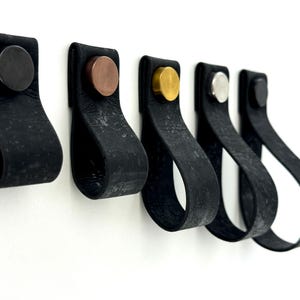 May include: Five black leather cabinet pulls with different colored metal accents. The pulls are in a row from left to right with black, copper, gold, silver, and black accents.