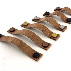 Könnte beinhalten: Sechs Kork-Schubladengriffe mit verschiedenen farbigen Metallakzenten. Die Griffe sind braun und haben eine strukturierte Oberfläche. Die Metallakzente sind schwarz, silber, gold, kupfer und messingfarben.