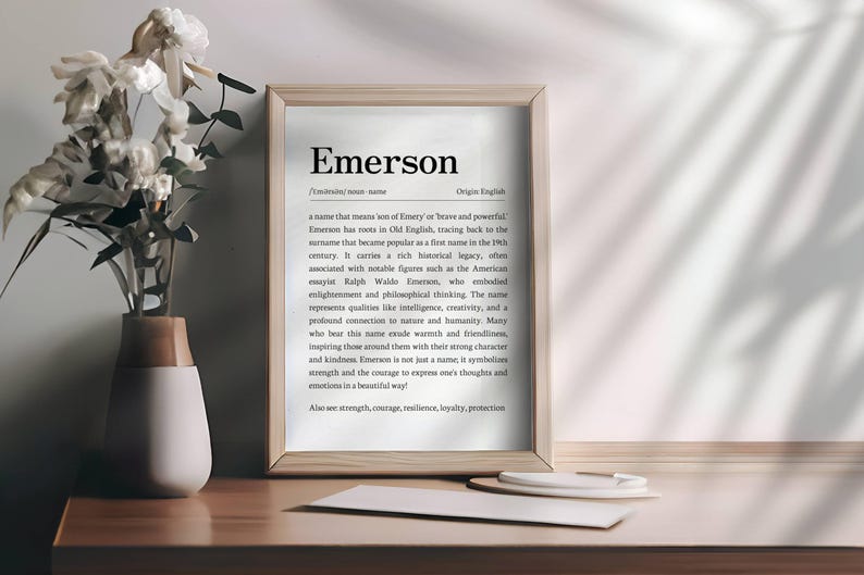 Peut inclure: Impression encadr&eacute;e avec le nom "Emerson" et sa d&eacute;finition. Un vase avec des fleurs blanches est &agrave; gauche. L'impression est sur une surface en bois. Le texte est en police serif.