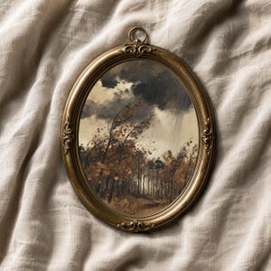 May include: An oval-shaped wall art piece featuring a landscape painting of a forest during a storm. The painting depicts dark, heavy clouds, rain, and trees with autumn-colored leaves bending in the wind. It is encased in an ornate gold frame.