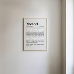 May include: A framed print with the name "Michael" in a serif font. The print includes a definition of the name, its origin, and associated qualities. The frame is a light wood color, and the background is white.
