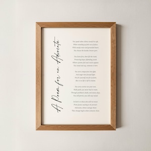 Puede incluir: Una impresión enmarcada con un marco de madera clara. La impresión presenta un poema titulado "A Poem for an Advocate" en elegante escritura negra sobre un fondo blanquecino. El texto del poema también es negro.