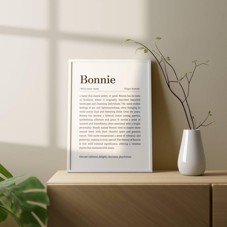 May include: A framed print with the name "Bonnie" in a minimalist design. The text describes the name's origin and meaning, with additional words like radiance, delight, charisma, and playfulness. A white vase with a plant is on the right.