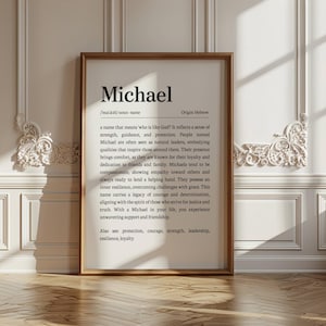 May include: A framed print with the name "Michael" in a black serif font. The print includes a definition, origin, and characteristics associated with the name. The frame is a warm brown color, and the background is a white wall with decorative molding.