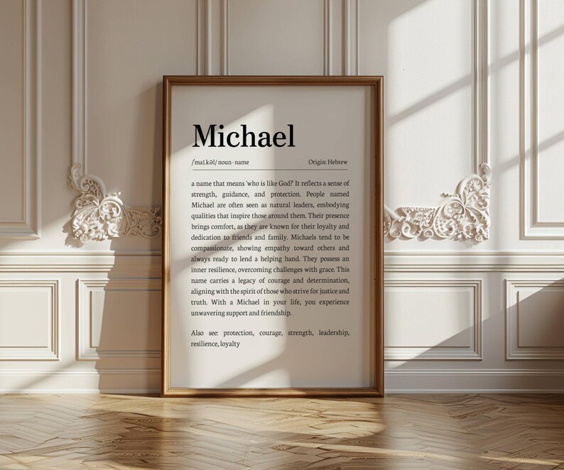May include: A framed print with the name "Michael" in a black serif font. The print includes a definition, origin, and characteristics associated with the name. The frame is a warm brown color, and the background is a white wall with decorative molding.