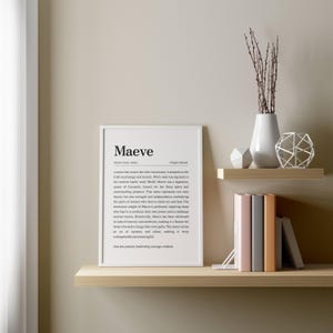 May include: A framed print with the name "Maeve" in a minimalist style, displayed on a wall with decorative shelves. The print includes a definition and origin. The shelves hold books, a white vase with branches, and geometric decor.