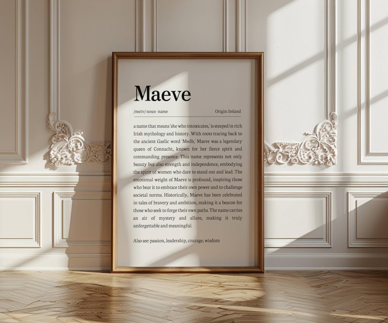 May include: A framed print with the name "Maeve" in a serif font. The text below describes the name's origin and meaning, including its connection to Irish mythology and the qualities it represents. The frame is a warm brown color.