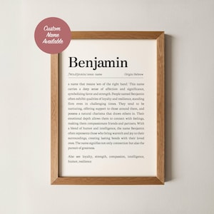 May include: A framed print displaying the name "Benjamin" in a black, sans-serif font. The print details the name's origin, meaning, and associated characteristics. A circular sticker in the top left corner says "Custom Name Available". The frame is light brown.