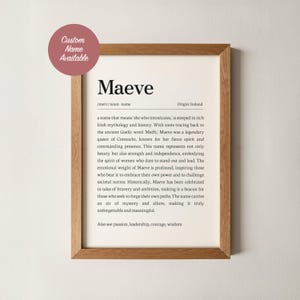 May include: A framed print with the name "Maeve" in a serif font. The print includes a definition, origin, and description of the name, with a wooden frame. A pink circle with the text "Custom Name Available" is in the upper left corner.