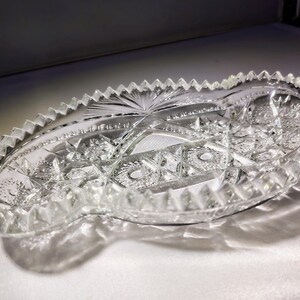 May include: A clear glass serving dish with a scalloped edge and intricate cut-glass design. The dish is oval shaped and has a delicate, ornate pattern.