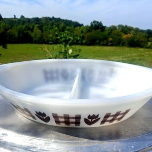 May include: A white milk glass divided serving dish with a central divider and integrated side handles. The exterior features a repeating brown pattern of stylized tulips and checkered squares encircling the base of the oval-shaped bowl.