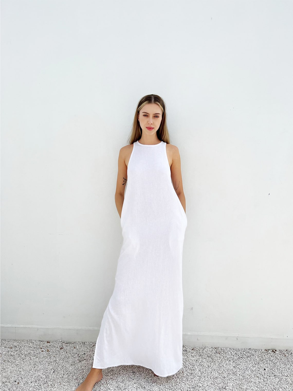 May include: A white sleeveless maxi dress with a high neckline and pockets. The dress is made of a lightweight fabric and has a relaxed fit.