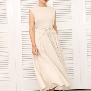 May include: A beige sleeveless maxi dress with a self-tie belt. The dress has a round neckline and a flowing skirt.
