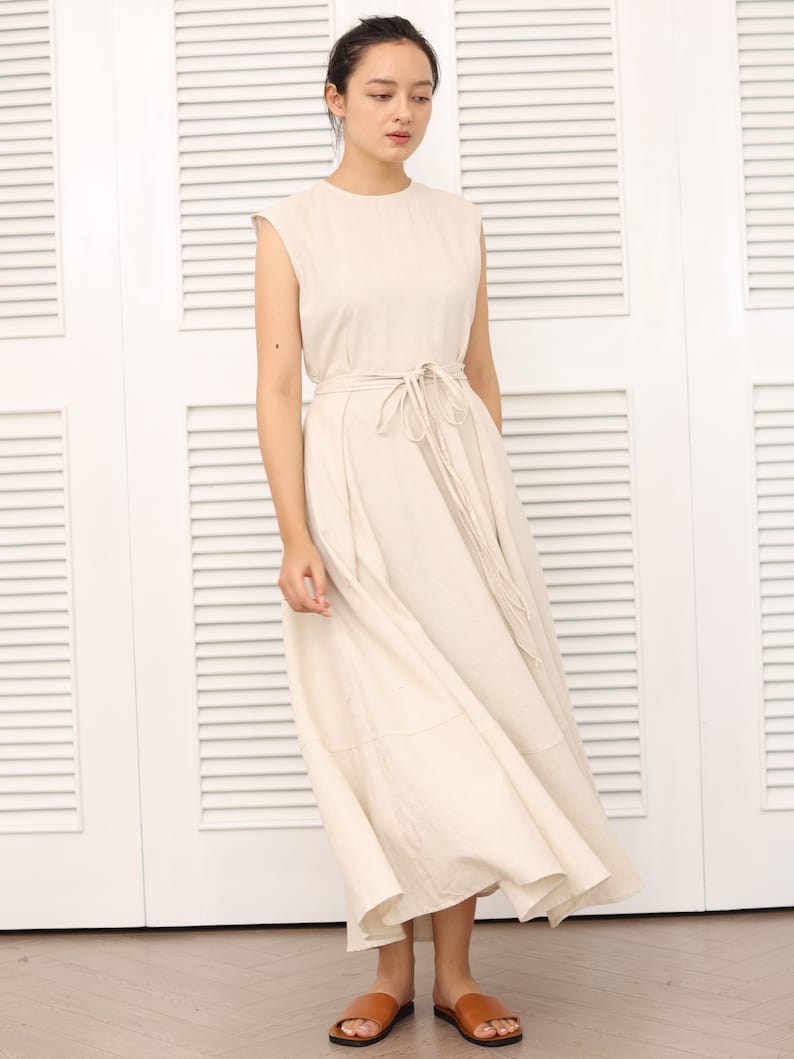 May include: A beige sleeveless maxi dress with a self-tie belt. The dress has a round neckline and a flowing skirt.