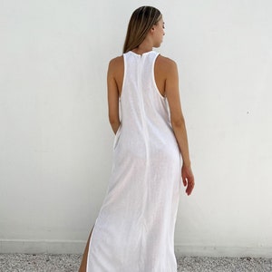 Puede incluir: Un vestido maxi blanco sin mangas con una cremallera en la parte posterior central. El vestido tiene una abertura lateral en el lado izquierdo.