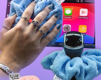 May include: A blue microfiber cleaning cloth is used to wipe a car screen. The text "Cleans your screens" is at the top. A blue scrunchie sits on the shifter. The text "Sits on Shifter" is at the bottom.