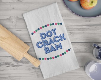 May include: White kitchen towel with a blue, green, and pink beaded border. The text "DOT CRACK BAM" is printed in blue on the towel.