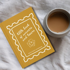 K&ouml;nnte beinhalten: Senfgelbes Buch mit dem Titel "little book of winners and losers" mit wei&szlig;em Zierrand und Spielkartenillustrationen. Neben dem Buch steht eine graue Tasse mit Kaffee auf einer wei&szlig;en Oberfl&auml;che.