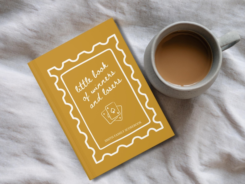 K&ouml;nnte beinhalten: Senfgelbes Buch mit dem Titel "little book of winners and losers" mit wei&szlig;em Zierrand und Spielkartenillustrationen. Neben dem Buch steht eine graue Tasse mit Kaffee auf einer wei&szlig;en Oberfl&auml;che.
