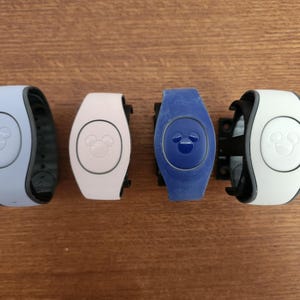 May include: Four Disney MagicBands in different colors: light blue, white, pink, and blue. Each band has a Mickey Mouse icon on the front.