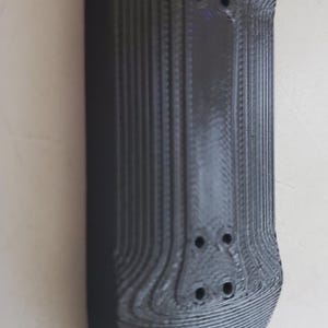 Puede incluir: Un fingerboard negro con una superficie texturizada y tres agujeros. El fingerboard está hecho de plástico y está diseñado para trucos de skate.