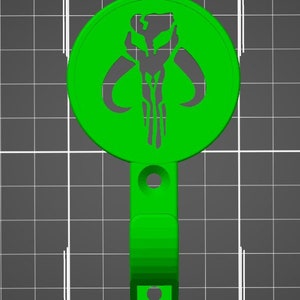 May include: Green plastic hook with a round Mandalorian symbol. The symbol is a skull with horns and a vertical line down the centre.
