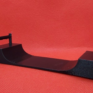 May include: Black plastic ramp with two rails at either end. The ramp is curved and has a textured surface.
