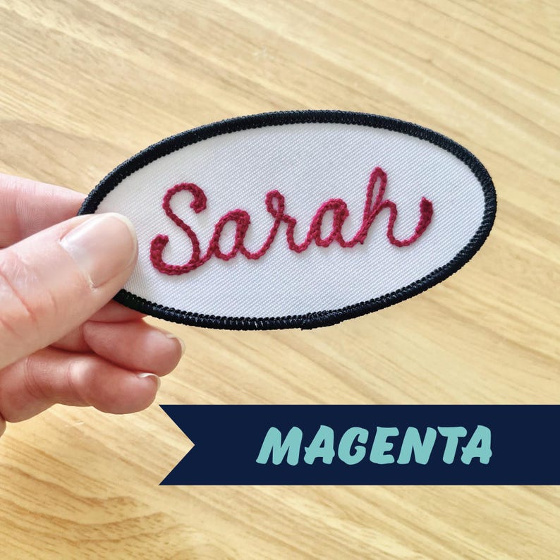 May include: White oval fabric patch with black stitching around the edges. The name "Sarah" is embroidered in red thread.