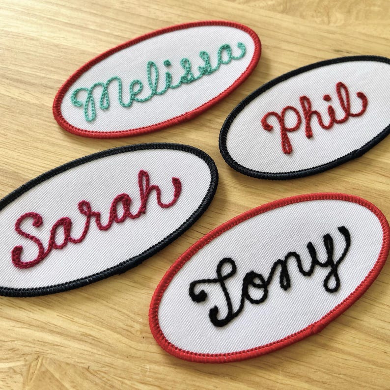 May include: Four white oval fabric patches with red and black trim. Each patch has a name embroidered in cursive lettering: Melissa, Phil, Sarah, and Tony.