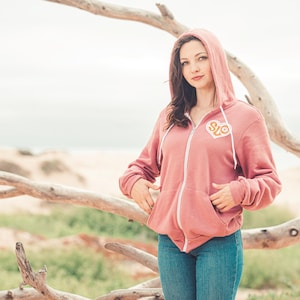 May include: A pink zip-up hoodie with a white zipper and a heart-shaped patch that says "SLO" in orange and white letters.