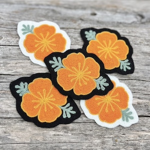 May include: Four embroidered felt patches with orange hibiscus flowers on a white background. The flowers have green leaves and are surrounded by a black border.