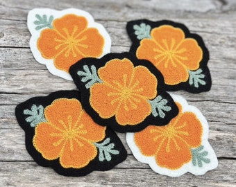 May include: Four embroidered felt patches with orange hibiscus flowers on a white background. The flowers have green leaves and are surrounded by a black border.