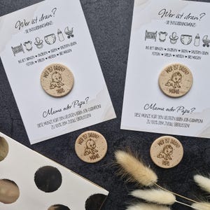 Könnte beinhalten: Hölzerne Baby-Entscheidungsmünzen mit dem Text "Wer ist dran?" und "Mama oder Papa?" werden auf Karten mit Baby-Symbolen angezeigt. Die Münzen zeigen eine Baby-Grafik und die Wörter "Papa" und "Mama".