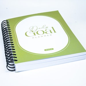 May include: A green and white daily goal planner with a spiral binding. The cover features the text "Daily Goal Planner" and the year "2024".