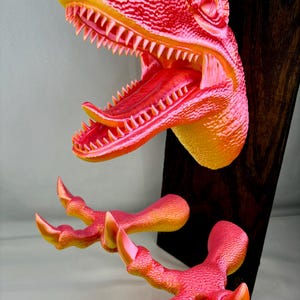 May include: A bright pink and orange dinosaur head wall mount with open mouth and sharp teeth. The dinosaur has two claws attached to the bottom of the mount.