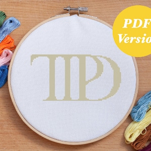 Peut inclure: Un projet de point de croix dans un cercle en bois, avec les lettres "TP" en beige clair. Le texte "PDF Version" est dans un cercle jaune. Des fils à broder colorés de différentes nuances entourent le cercle.