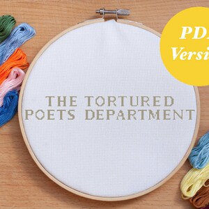 May include: A white embroidery hoop with the text "THE TORTURED POETS DEPARTMENT" printed on it.  The hoop is surrounded by colorful embroidery floss.