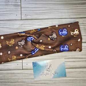 Pu&ograve; includere: Fascia per capelli in tessuto marrone con un motivo a pixel di galline e uova. La fascia &egrave; attorcigliata e presenta un design di gallina pixelato blu e bianco.