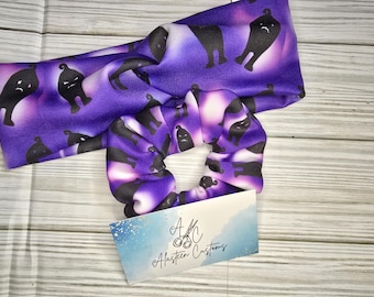 Può includere: Un elastico per capelli viola e bianco con una stampa di gatto nero. Lo scrunchie è abbinato a una fascia per capelli abbinata. Sia la fascia che lo scrunchie sono realizzati in tessuto morbido ed elastico. Il testo "A/C Alasteen Customs" è stampato su una carta bianca.