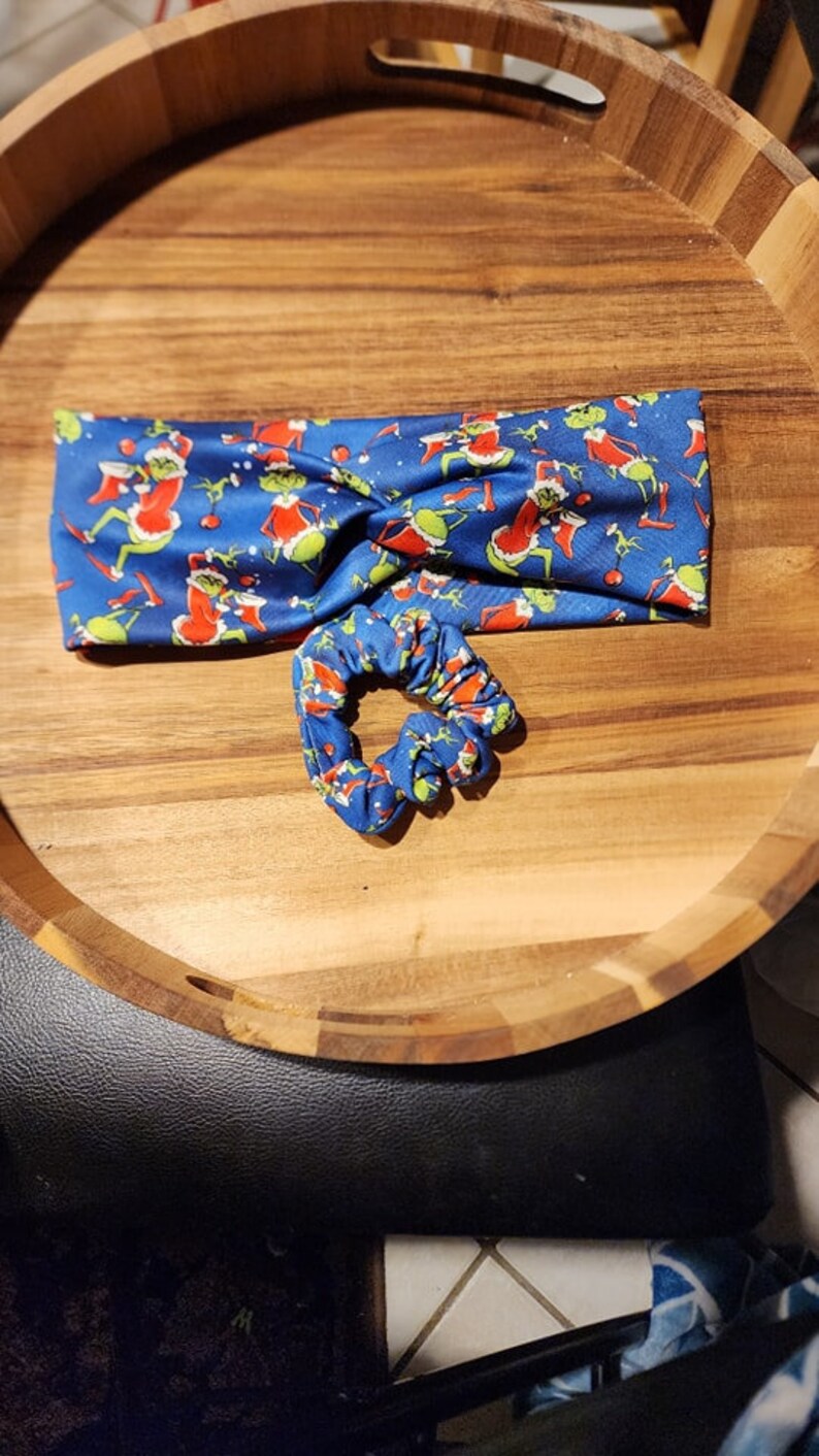Op de afbeelding: Een blauw hoofdband met een kerstthema print van groene en rode figuren. Een bijpassende blauwe scrunchie is ook inbegrepen.