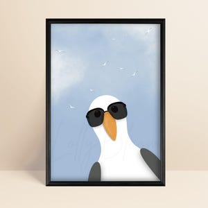 May include: A framed wall art print featuring a white and gray seagull wearing black sunglasses against a light blue sky with clouds and small birds. The bird has a prominent orange beak and is positioned in the lower center of the frame.