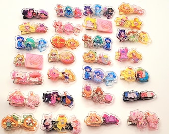 以下が含まれることがあります： アニメスタイルのキャラクターが特徴的な、カラフルなアクリルヘアクリップのコレクション。ピンク、ブルー、イエロー、パープルのアクセントが施された様々なデザイン。各クリップは約5cmの長さで、金属製の留め金が付いています。